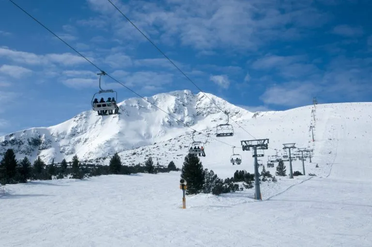 Panoramic wide angle view on white snowy ski slopes , mountain peak and ski chairlift transporting skiers.